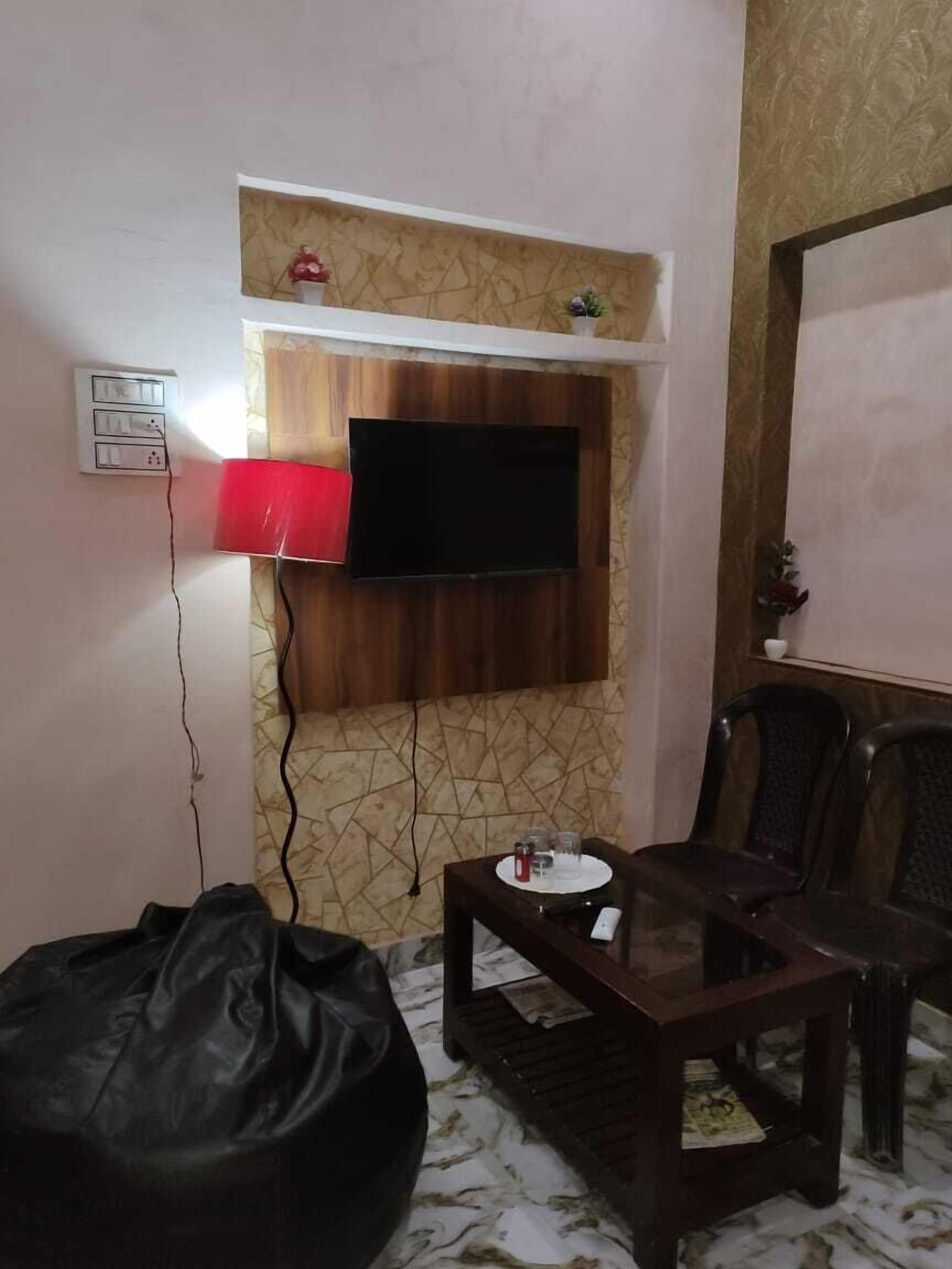 A living room with a TV mounted on a patterned wall, a red lamp, a small table with glasses, and a bean bag chair.