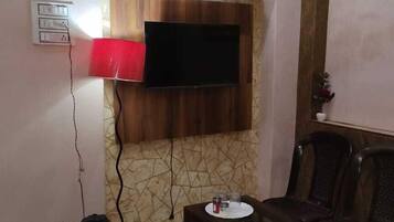 A living room with a TV mounted on a patterned wall, a red lamp, a small table with glasses, and a bean bag chair.