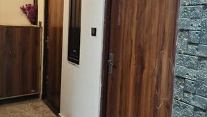 A hallway with two wooden doors, one with a black frame and the other with a natural wood finish. The walls are white, and there is a stone-textured accent wall on the right. - Kashiyana Stay (Varanasi)