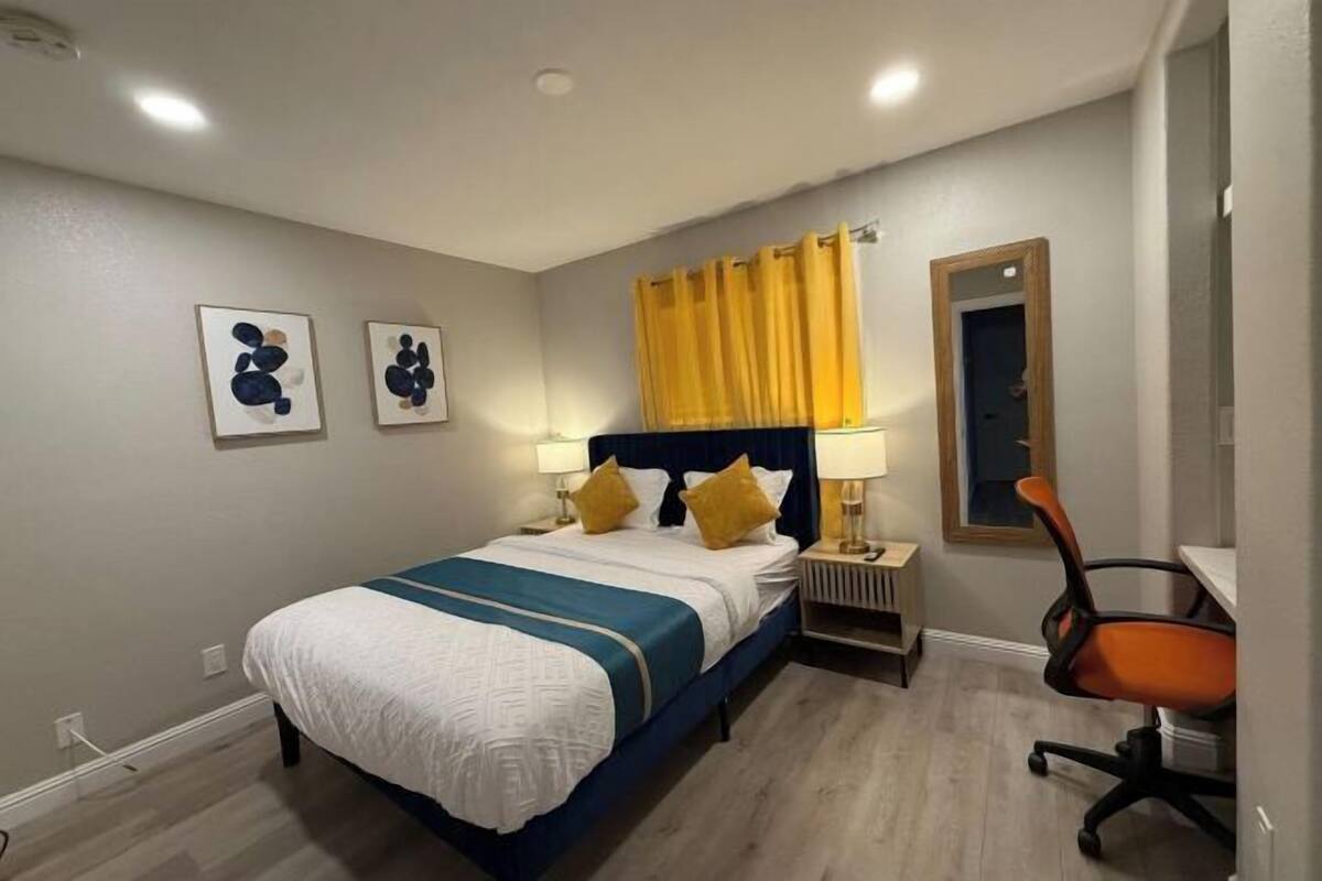 A hotel room with a bed, bedside tables, a chair, and artwork on the wall.