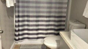 Un baño con cortina de ducha a rayas, inodoro y lavamanos blanco.