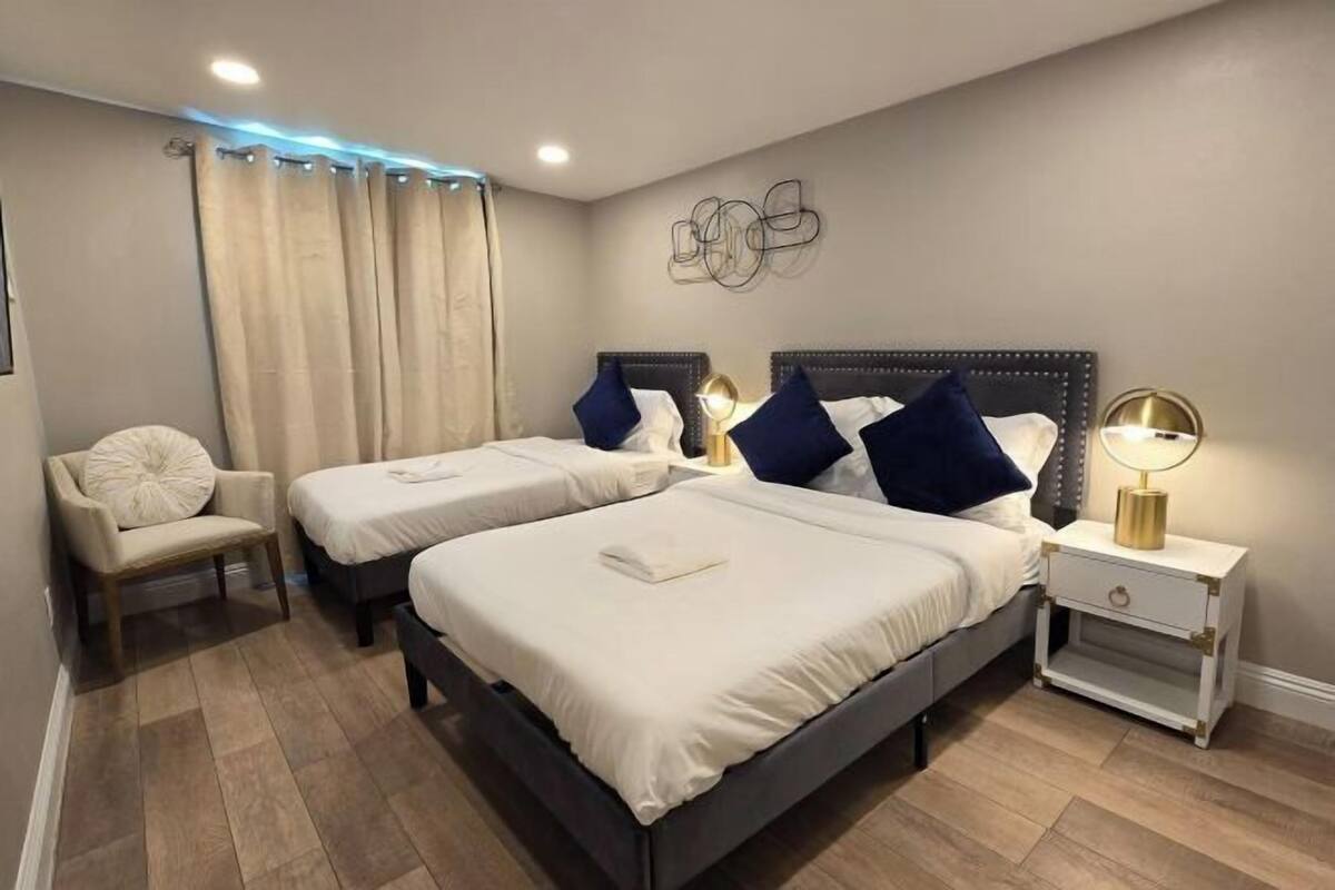 A hotel room with two beds, a chair, and a nightstand with a lamp.
