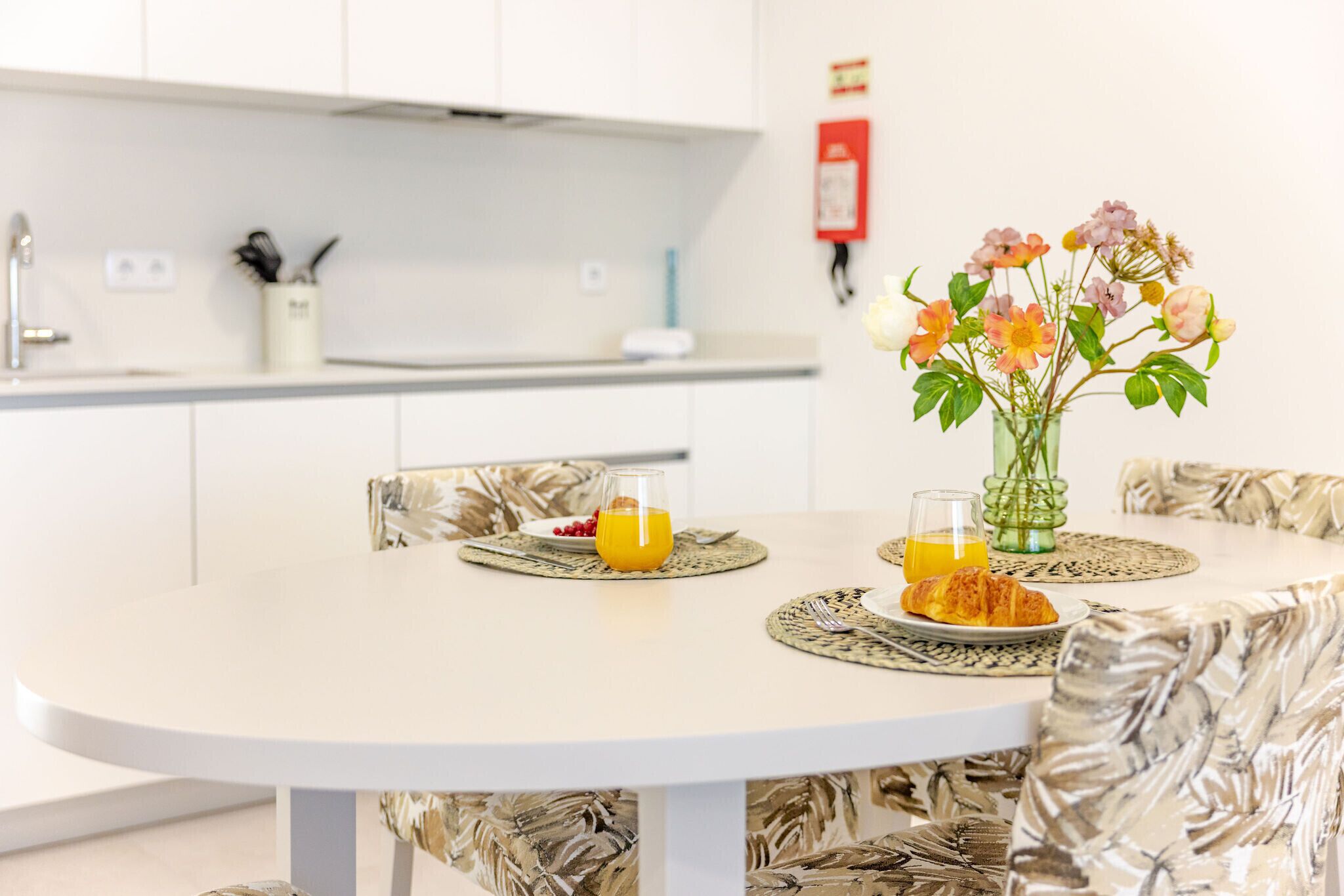 Een ronde eettafel met een wit tafelkleed, een vaas met bloemen en een croissant op een bord.