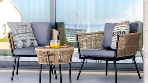 A modern outdoor seating area with wicker chairs and a round table, featuring a glass partition and a view of the sea. - Vale Furado Sea & Nature - BY SCH (Nazaré)