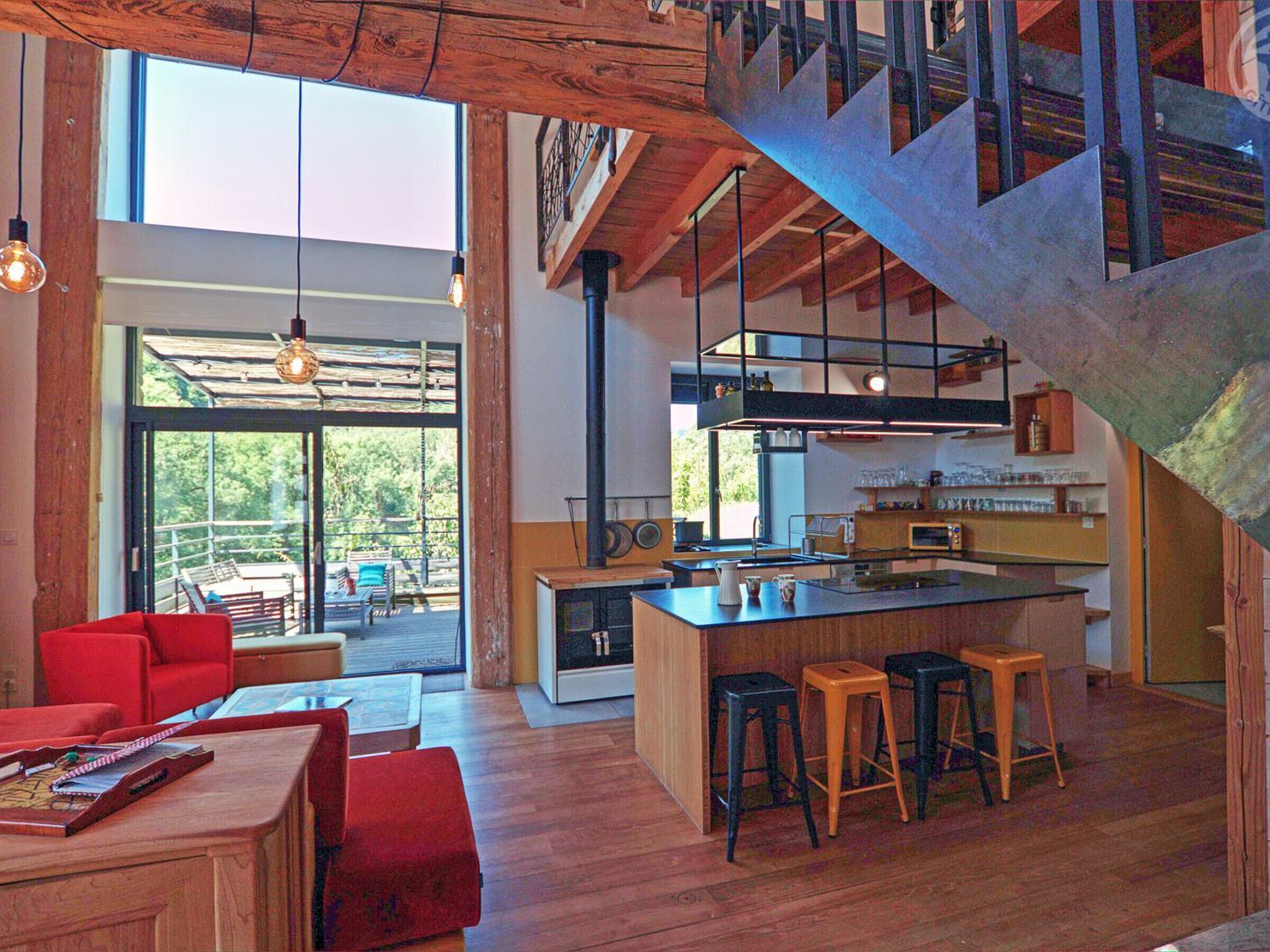A spacious living area with a wooden floor, a red sofa, a coffee table, and a kitchen with a central island and stools.