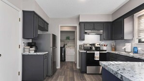 Une cuisine moderne avec des meubles de couleur sombre, un réfrigérateur en acier inoxydable, un four encastré et un plan de travail en granit.