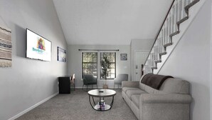 Un salon moderne avec un canapé gris, une table basse ronde et un escalier doté de balustrades blanches.