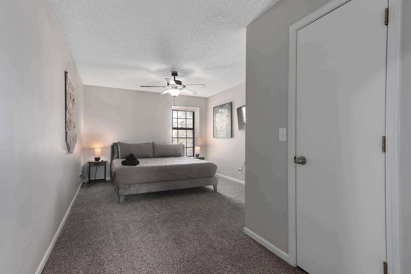 A bedroom with a bed, a ceiling fan, a window, and a door.