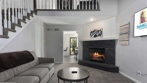 Un salon moderne avec un canapé gris, une table basse ronde, une cheminée et un escalier doté de balustrades blanches.
