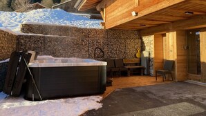 Una cabaña de madera con pared de piedra, un jacuzzi y mobiliario exterior.