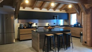 Una cocina moderna con vigas de madera, una isla central con taburetes y un refrigerador de acero inoxidable.