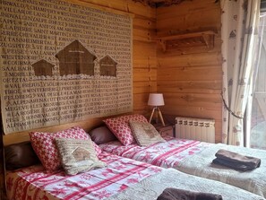 Ein gemütliches Cabin-Zimmer mit einem Bett, das eine gemusterte Tagesdecke hat, einer Wand mit einer Namensliste und einem Fenster mit Vorhängen.