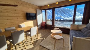 Une chambre moderne avec des murs en bois, une télévision, un coin repas, un canapé et de grandes fenêtres offrant une vue sur la montagne.