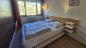Une chambre moderne avec un grand lit, des tables de chevet, une fenêtre donnant sur un espace verdoyant et un tableau au mur.