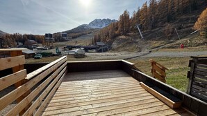 En træterrasse med udsigt over et bjerglandskab, en stolelift og bygninger i baggrunden.