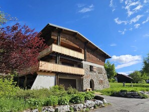 A two-story chalet with a stone base and wooden upper levels, featuring balconies and a garage. - Renovated family chalet, near center, sleeps 12, parking, WiFi (Les Gets)