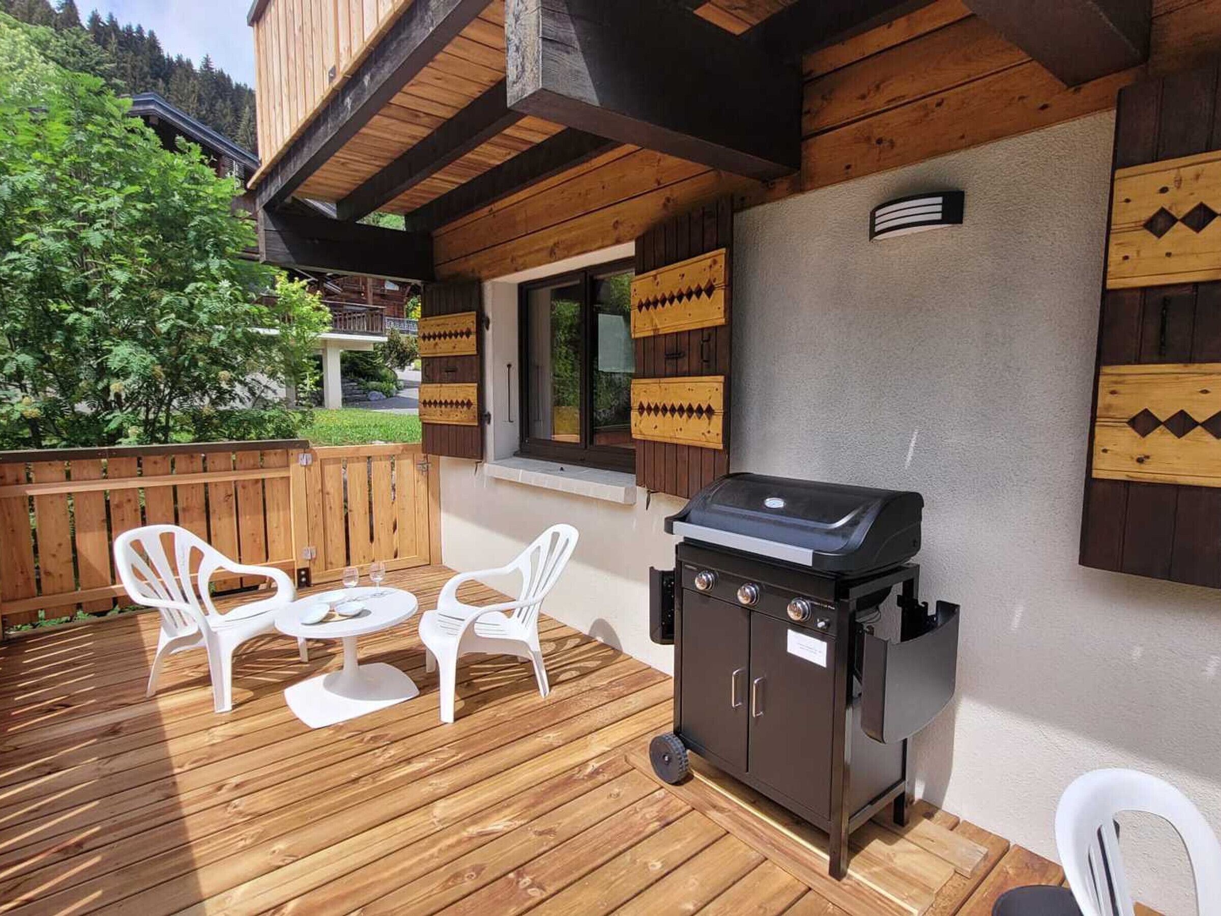 An outdoor patio with a grill, white plastic chairs, and a wooden deck.