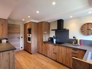 A modern kitchen with wooden cabinets, a black range hood, a built-in microwave, and a round wall clock. - Renovated family chalet, near center, sleeps 12, parking, WiFi (Les Gets)