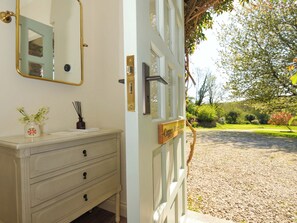 Una puerta con un letrero que dice 'Copper Mine Cottage', un espejo, un jarrón con flores y un aparador de madera con cajones.