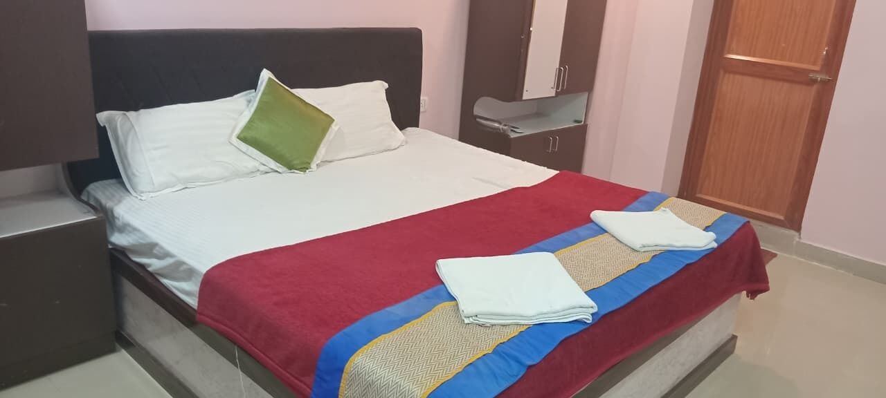 A neatly made bed with a red and blue bedspread, white pillows, and a green accent pillow.