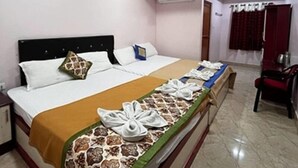 A hotel room with a large bed, a desk, and a chair. There is an air conditioning unit on the wall and a ceiling fan. - Elite Square  (Port Blair)