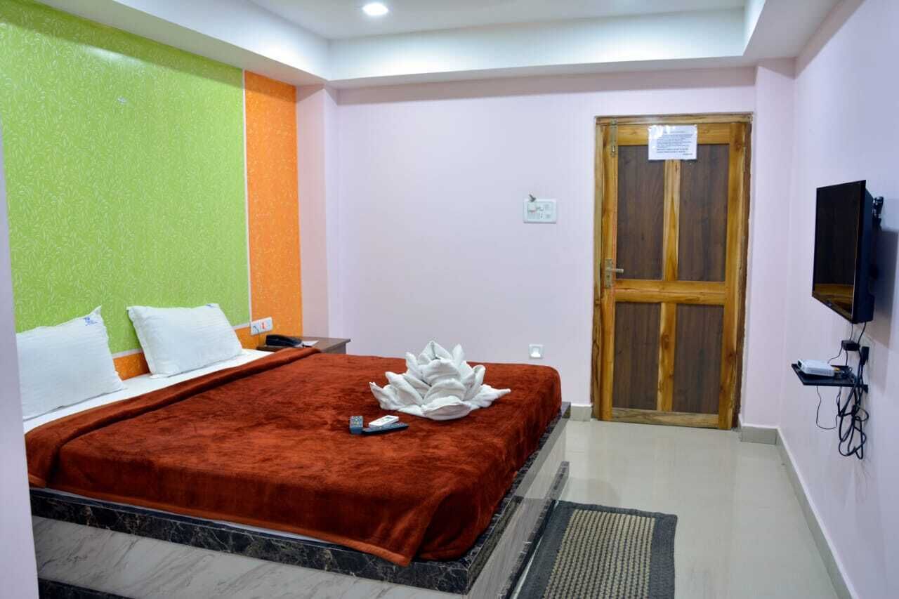 Una habitación de hotel con una cama, una puerta de madera, un televisor y un estante fijado a la pared.