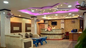 A hotel reception area with a reception desk, a sofa, a blue table, and a TV screen. - Elite Square  (Port Blair)