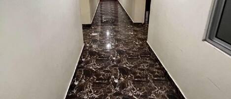 Un pasillo con paredes blancas, piso de mármol y una lámpara en el techo.