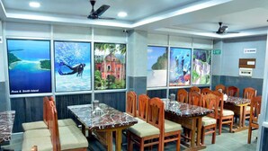 A restaurant with wooden tables and chairs, large windows with scenic views, and a 'No Smoking' sign. - Elite Square  (Port Blair)