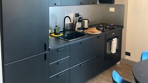 Moderni keittiö, jossa on tummat kaapit, musta työtaso, pesuallas, liesi ja pieni uuni.