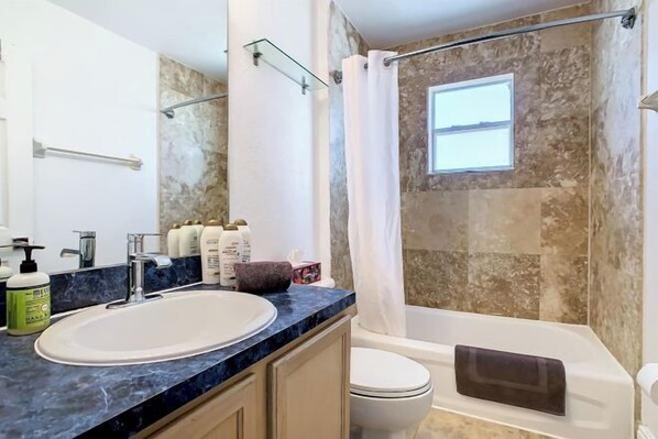 A bathroom with a sink, toilet, and bathtub, featuring a stone wall and a window. - DisneyMansion by AmericanVacationLiving 11Br - 30p (Davenport)