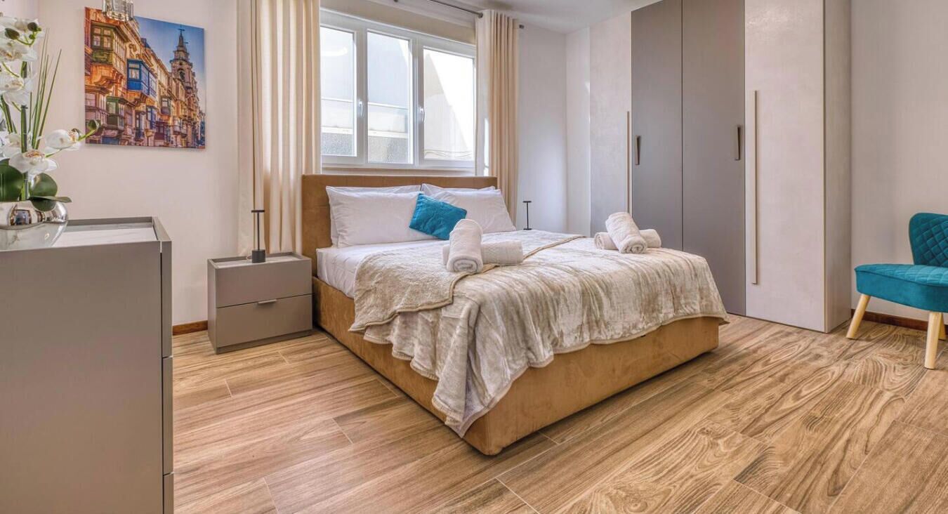 A modern bedroom with a large bed, a nightstand, a wardrobe, and a chair.