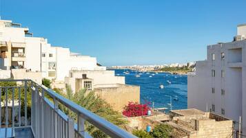 A coastal residential area with white buildings, a clear blue sky, and a view of the sea with boats.