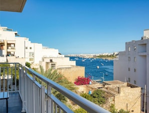 A coastal residential area with white buildings, a clear blue sky, and a view of the sea with boats. - Equipped Seafront 2BR APT close promenade w/WIFI (St. Paul`s Bay)