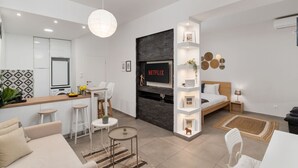 Een moderne woonkamer met een bank, een eethoek met stoelen, een keuken met een koelkast en een tv aan de muur.