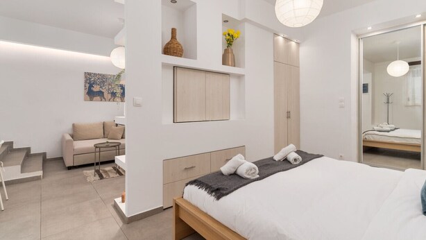 Een moderne slaapkamer met een groot bed, een inbouw kast, een zithoek met een sofa en een klein tafeltje.