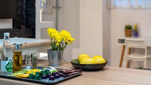 Een aanrecht met een metalen vaas vol gele bloemen, een schaal met citroenen en een dienblad met kleurrijke capsules.