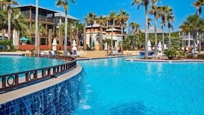 Zwembad met ligbedden en palmbomen, omringd door resortgebouwen.