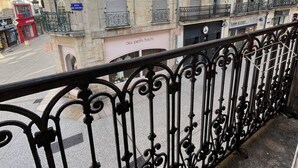 Ein Balkon mit schmiedeeisernen Geländern mit Blick auf eine Straße mit Gebäuden, darunter ein Geschäft mit der Aufschrift 'des petits hauts'.