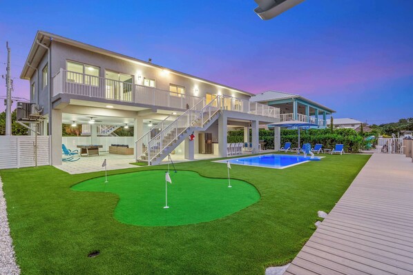 A two-story house with a pool, a covered patio, and a well-maintained lawn.