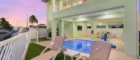 A pool area with lounge chairs and a staircase leading to an upper level.
