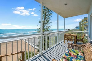 A balcony with a view of the ocean, a wicker sofa, and a wooden table. - Oceanfront 2BR-Perfect Beach View Balcony (Satellite Beach)