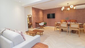 A modern living room with a sofa, coffee table, dining table with chairs, and a TV mounted on the wall. - Elegant Apartment St Germain des prés Luxembourg Park (Paris)