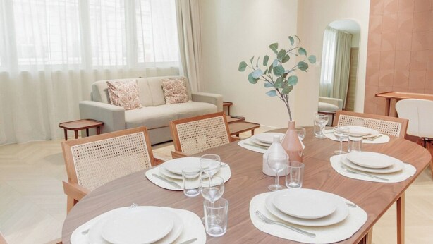 A dining area with a wooden table set for four, surrounded by wicker chairs. A sofa and a small side table are visible in the background. - Elegant Apartment St Germain des prés Luxembourg Park (Paris)