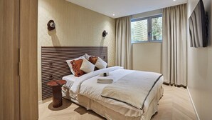 A modern bedroom with a wooden headboard, a bedside table, a large window with curtains, and a flat-screen TV mounted on the wall. - Elegant Apartment St Germain des prés Luxembourg Park (Paris)