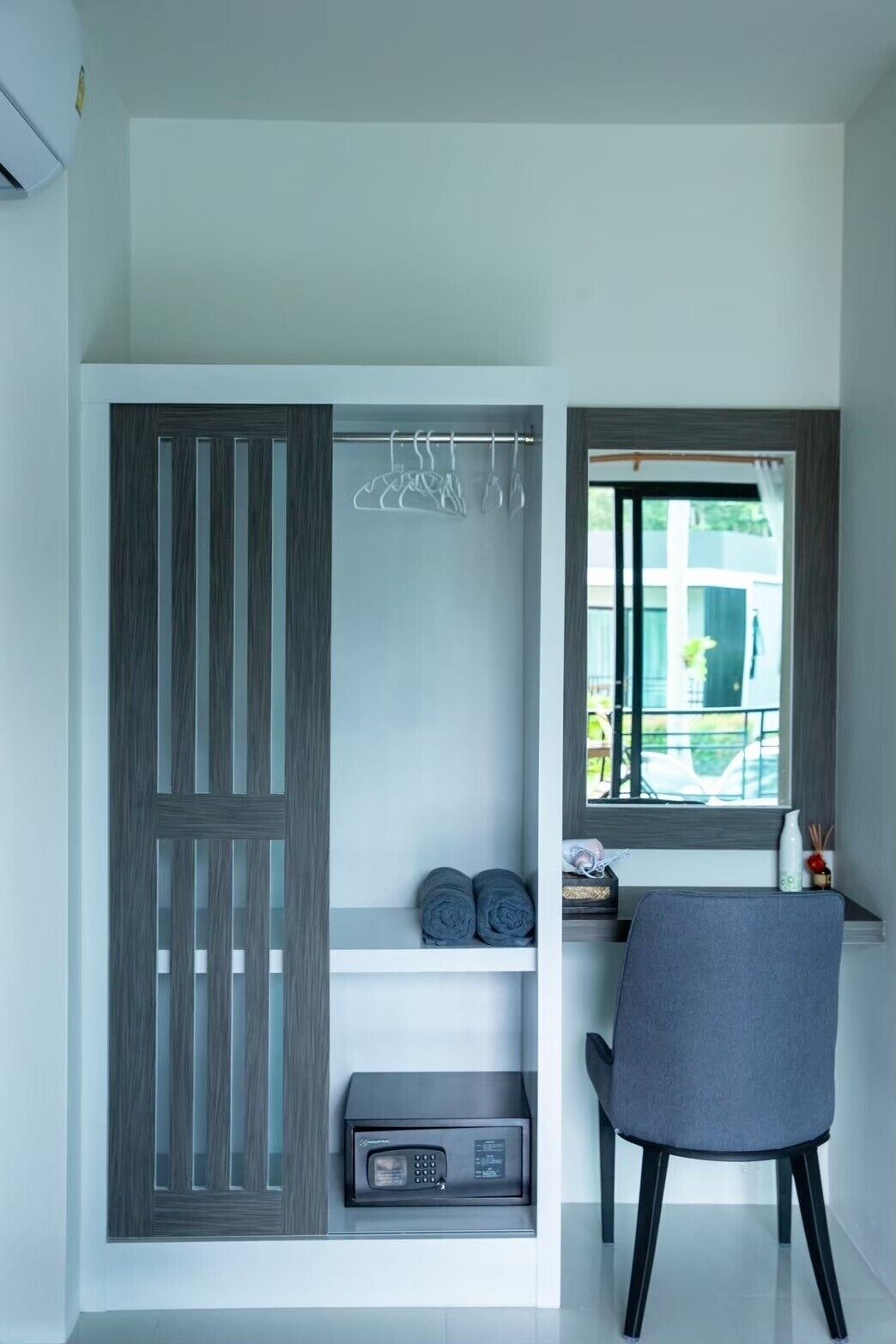 A compact room with a built-in wardrobe, a microwave, a chair, and a window with a view of greenery.