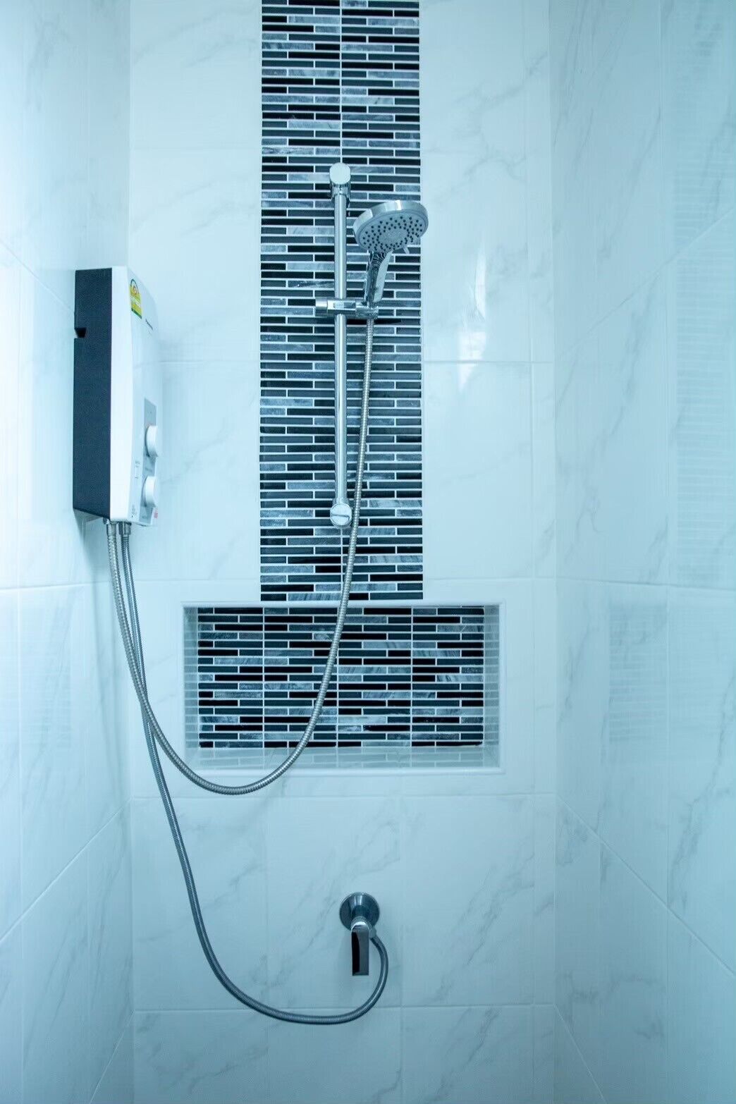 A bathroom with a shower, a control panel, and a ventilation grille.
