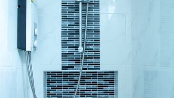 A bathroom with a shower, a control panel, and a ventilation grille.