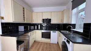 A modern kitchen with light wood cabinets, black countertops, a built-in oven, a dishwasher, a washing machine, and a window with a view. - Urban Calm – Spacious 3-Bed Home with Free Parking
• Self Check-In (Rawmarsh)