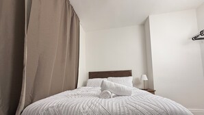 A neatly made bed with a striped bedspread and pillows, a bedside lamp, and a hanging coat rack. - Urban Calm – Spacious 3-Bed Home with Free Parking
• Self Check-In (Rawmarsh)
